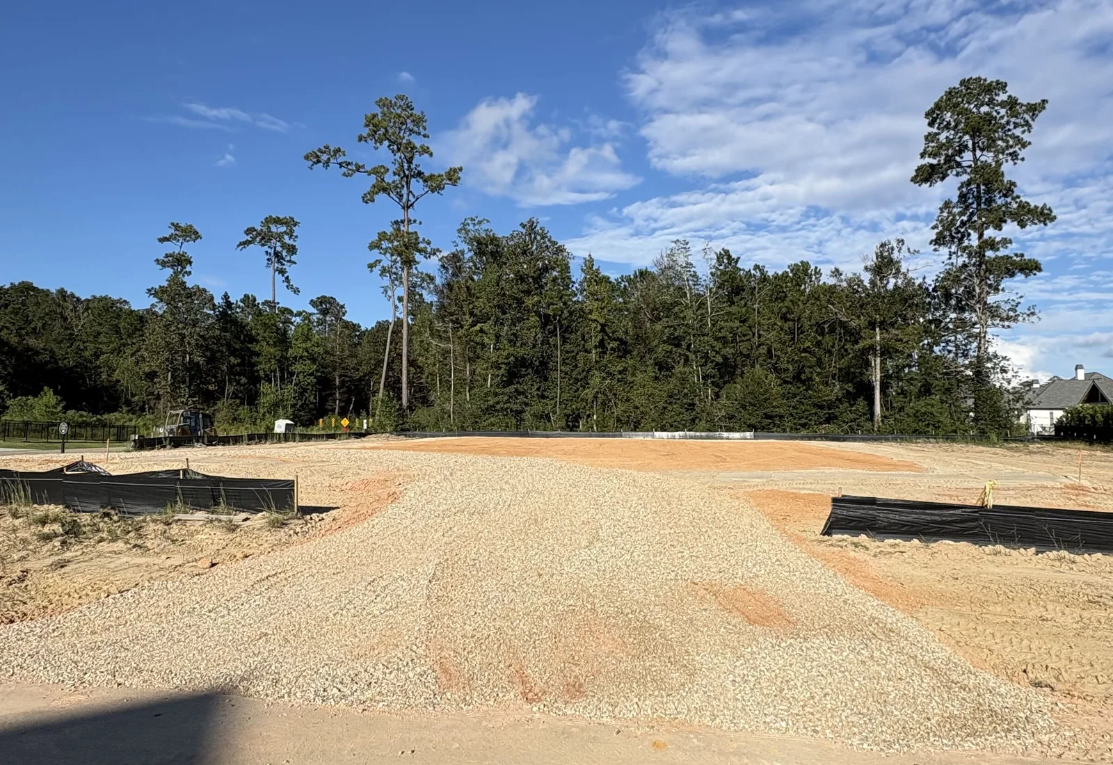 Crushed limestone gravel spread over a sand pad between two silt fences, pines and a house behind
