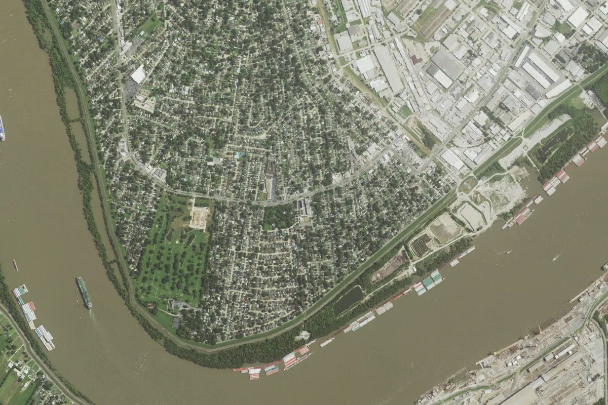 Aerial view of Harahan's tree-lined neighborhoods inside a bend of the Mississippi River, with the levee and barges along the bank