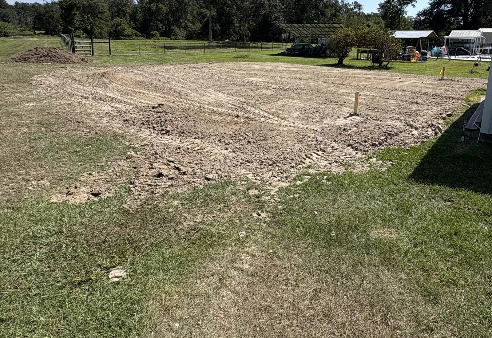 Freshly graded dirt pad in a grass yard beside a metal building