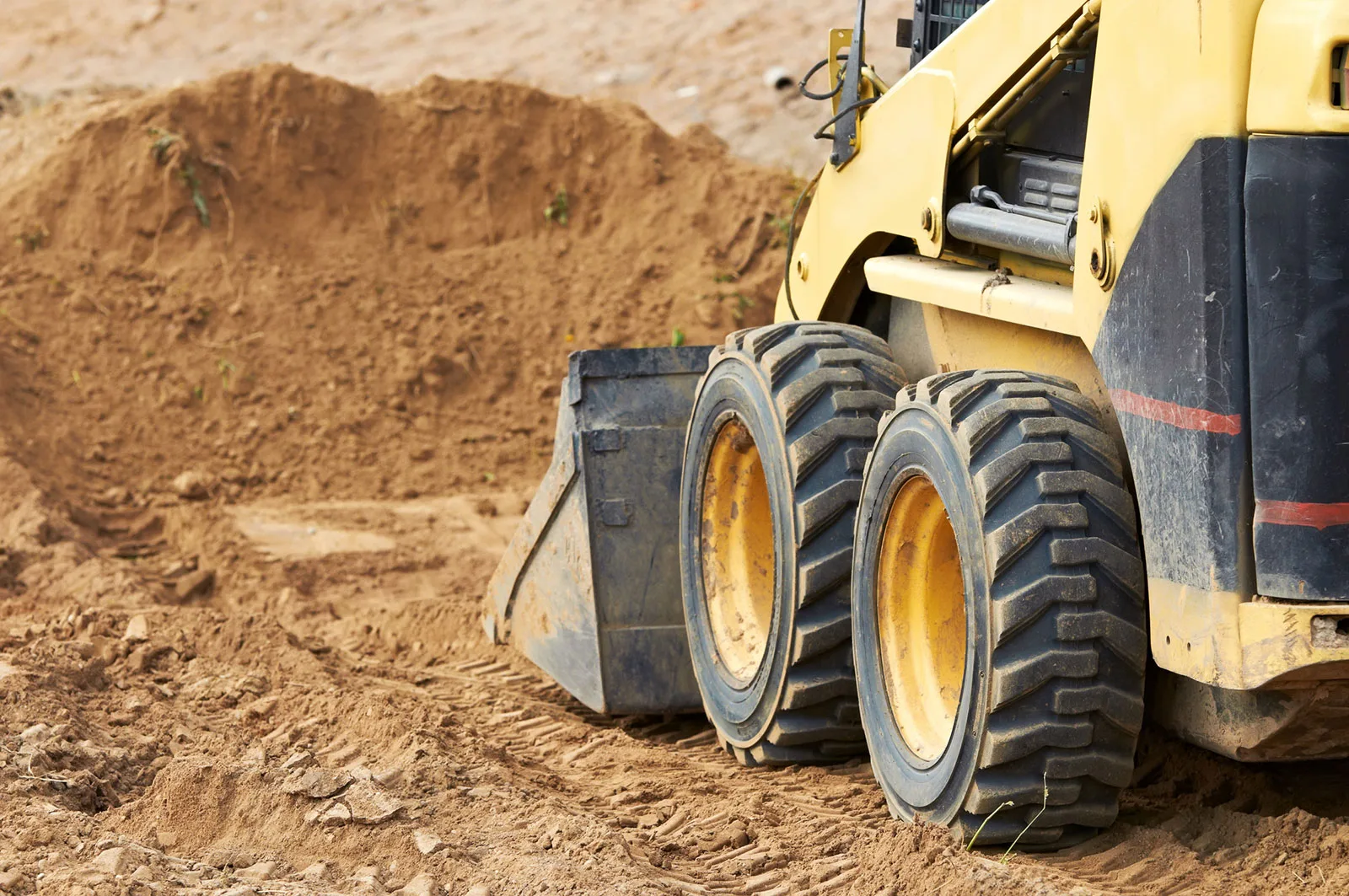 Skid steer bucket at a pile of loose dirt